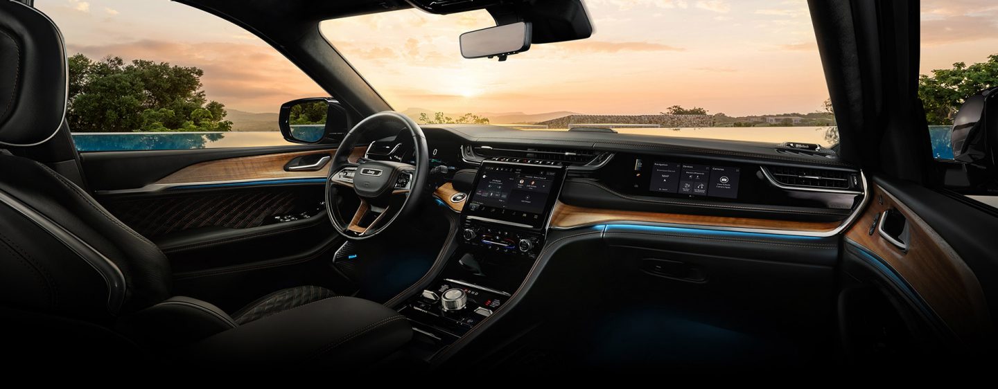 The cockpit of the Jeep Grand Cherokee Summit Reserve with a view of a lake at sunset through the windshield.